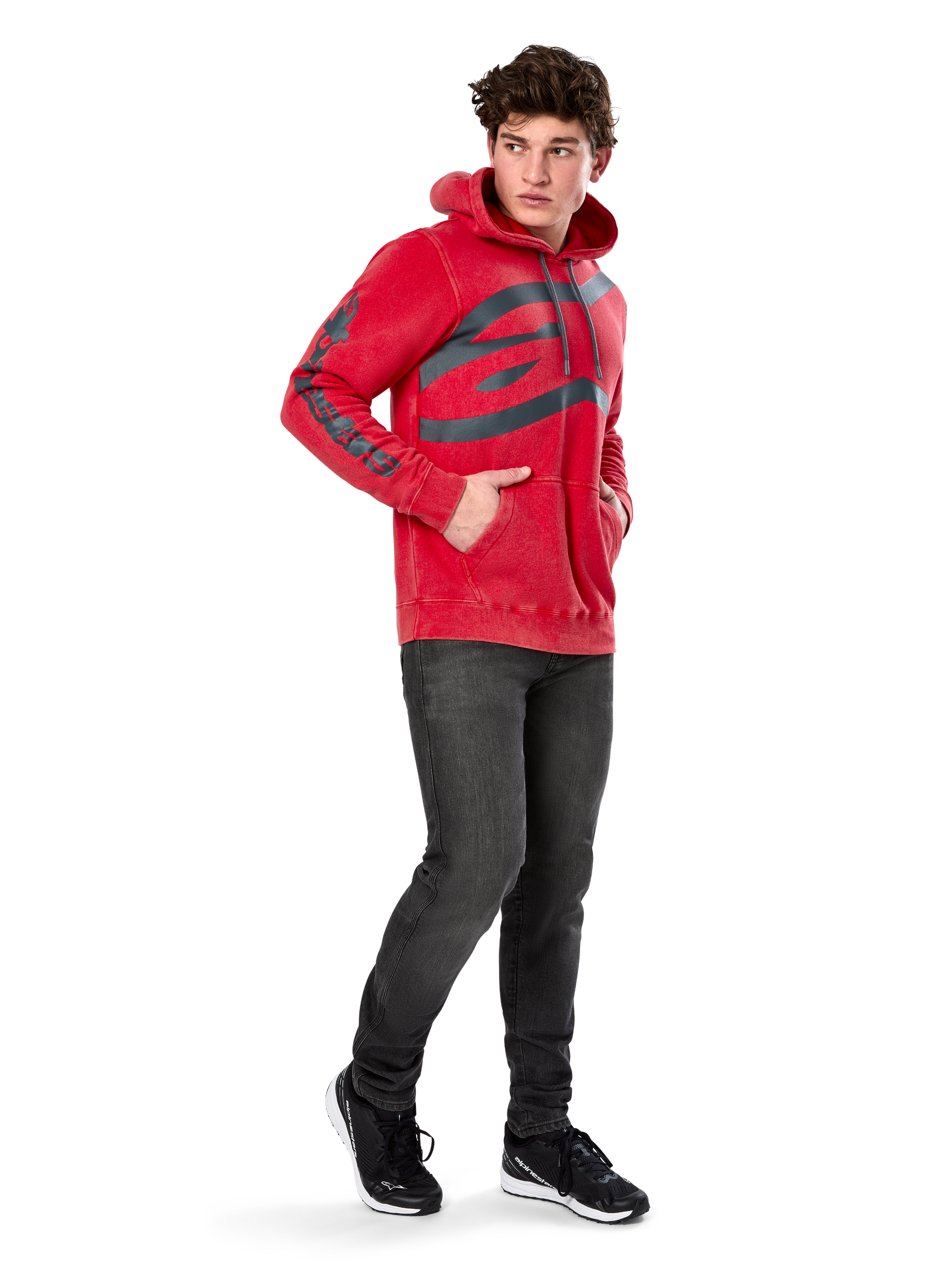 Alpinestars Unbound Hoodie, Red garment-dyed pullover fleece, extra-large dark logo on chest and wordmark on sleeves, kangaroo pocket, drawstring hood, worn by model with dark gray jeans and black sneakers, casual motorsport-inspired streetwear