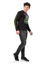 Man wearing Alpinestars Ayess CSF Long Sleeve Tee, Black, featuring yellow sleeve lettering and vibrant lime and cyan chest graphics, paired with dark grey jeans and black sneakers, casual motorsport-inspired streetwear.