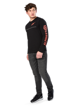 Male model wearing Alpinestars Committed CSF Tee, Long Sleeve T-Shirt, Black, orange-red chest logo and sleeve branding, paired with dark gray jeans and black sneakers, casual motorsport-inspired streetwear