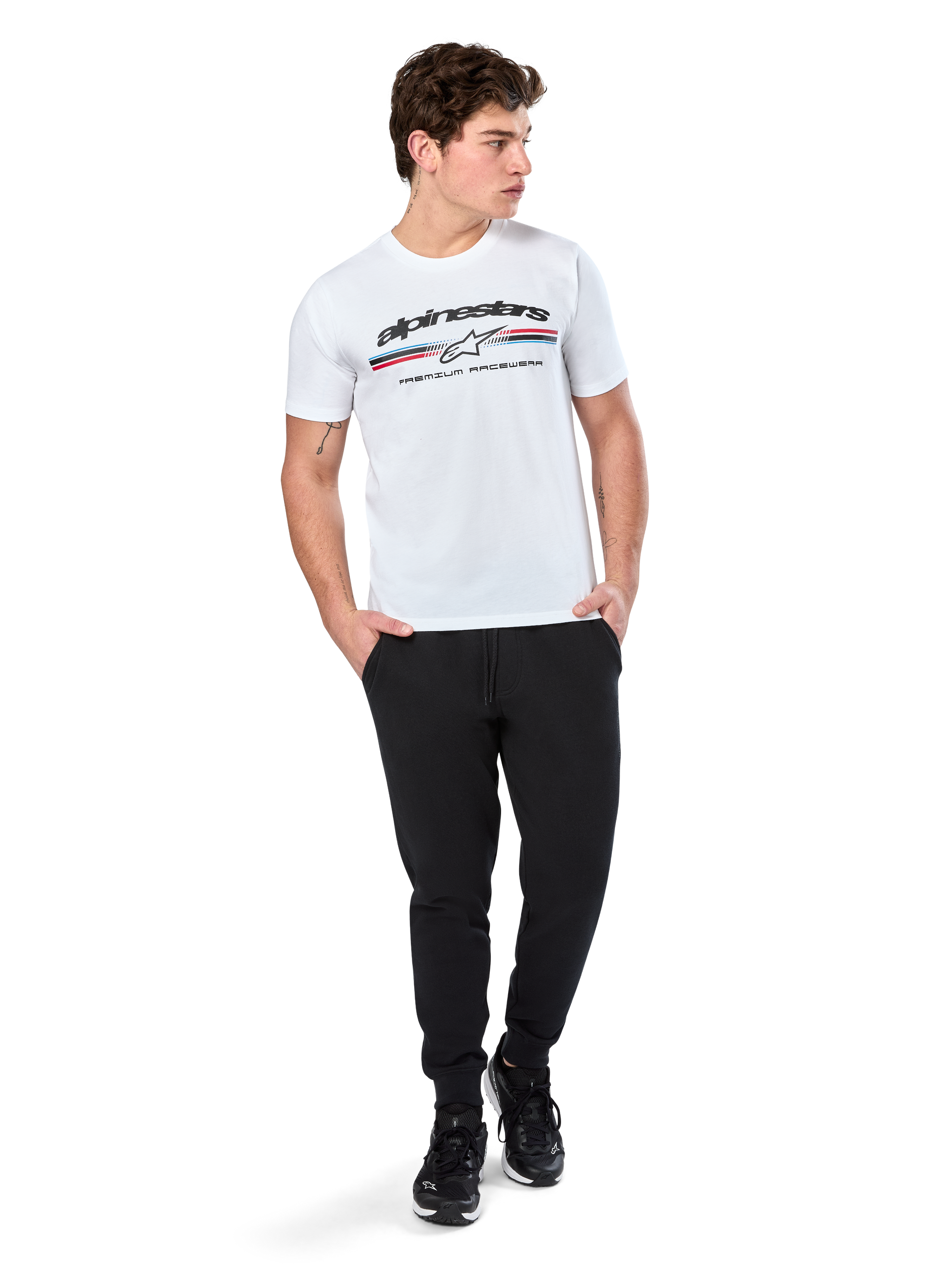 Alpinestars Prevail CSF Tee, Short Sleeve T-Shirt, White, featuring a front paddock-style tri-color stripe logo with Alpinestars branding, worn by a model with black joggers and black sneakers, casual motorsport streetwear
