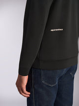 Alpinestars Cypher Hoodie, close-up view of the lower back and sleeve, Black double-face fleece with white Alpinestars word logo, worn with blue jeans, casual motorsport streetwear