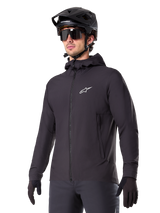 Alpinestars A-Dura Thermal Jacket, Black Cycling Jacket, hooded design with front zipper, white star logo on chest, worn with black mountain bike helmet and gloves, sporty performance gear for cold weather trail riding
