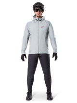 Alpinestars A-Dura Thermal Jacket, Titanium gray, cycling jacket worn with black mountain biking pants, gloves, and helmet, featuring a small red star logo on the chest and a full front zipper, lightweight insulated gear for off-road riding.