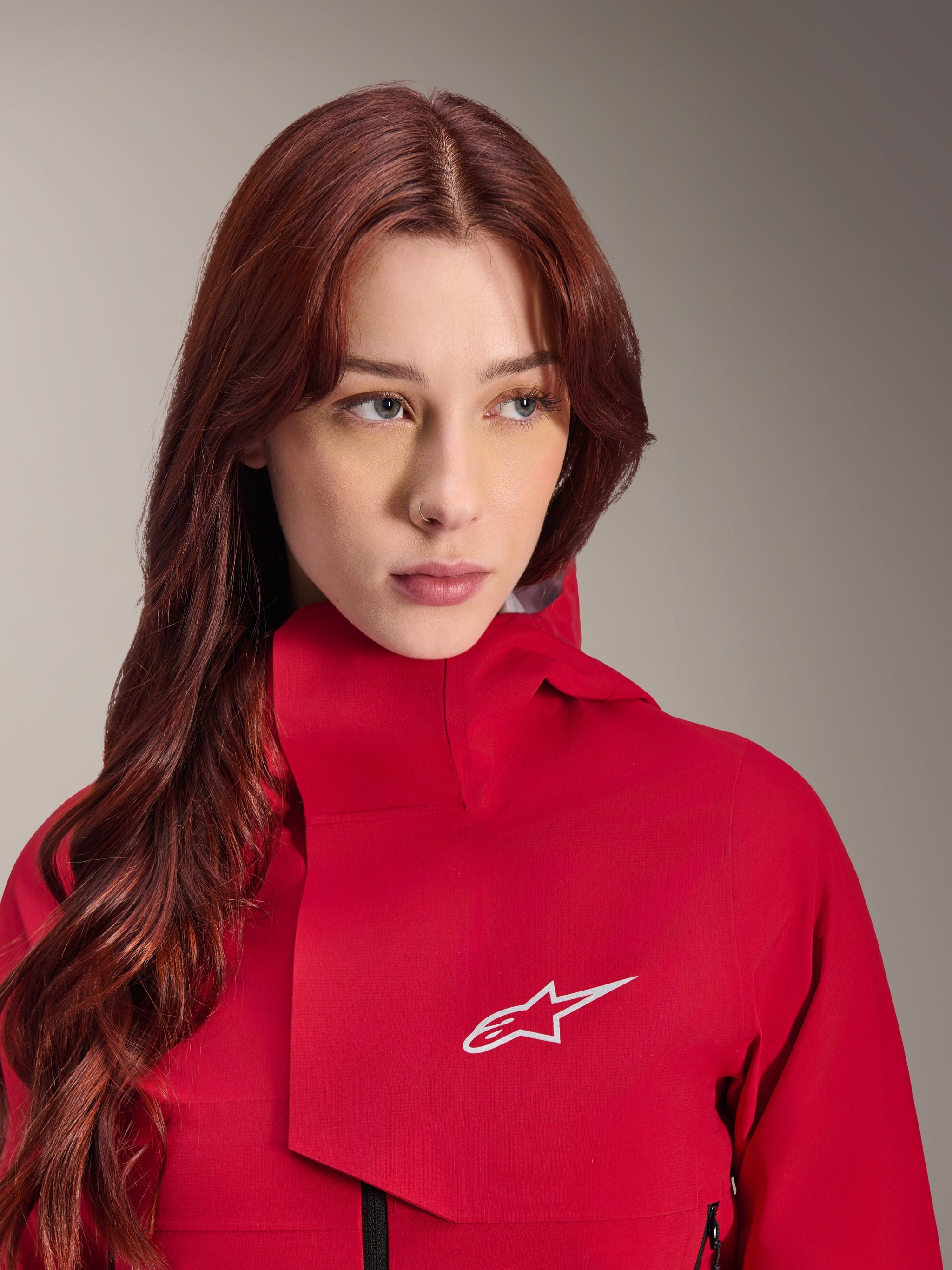 Alpinestars Stella A-Dura Elite Waterproof Jacket, Red Fluo, worn by a woman with long red hair, technical 3-layer waterproof jacket with high collar and white logo, performance outdoor and mountain bike gear