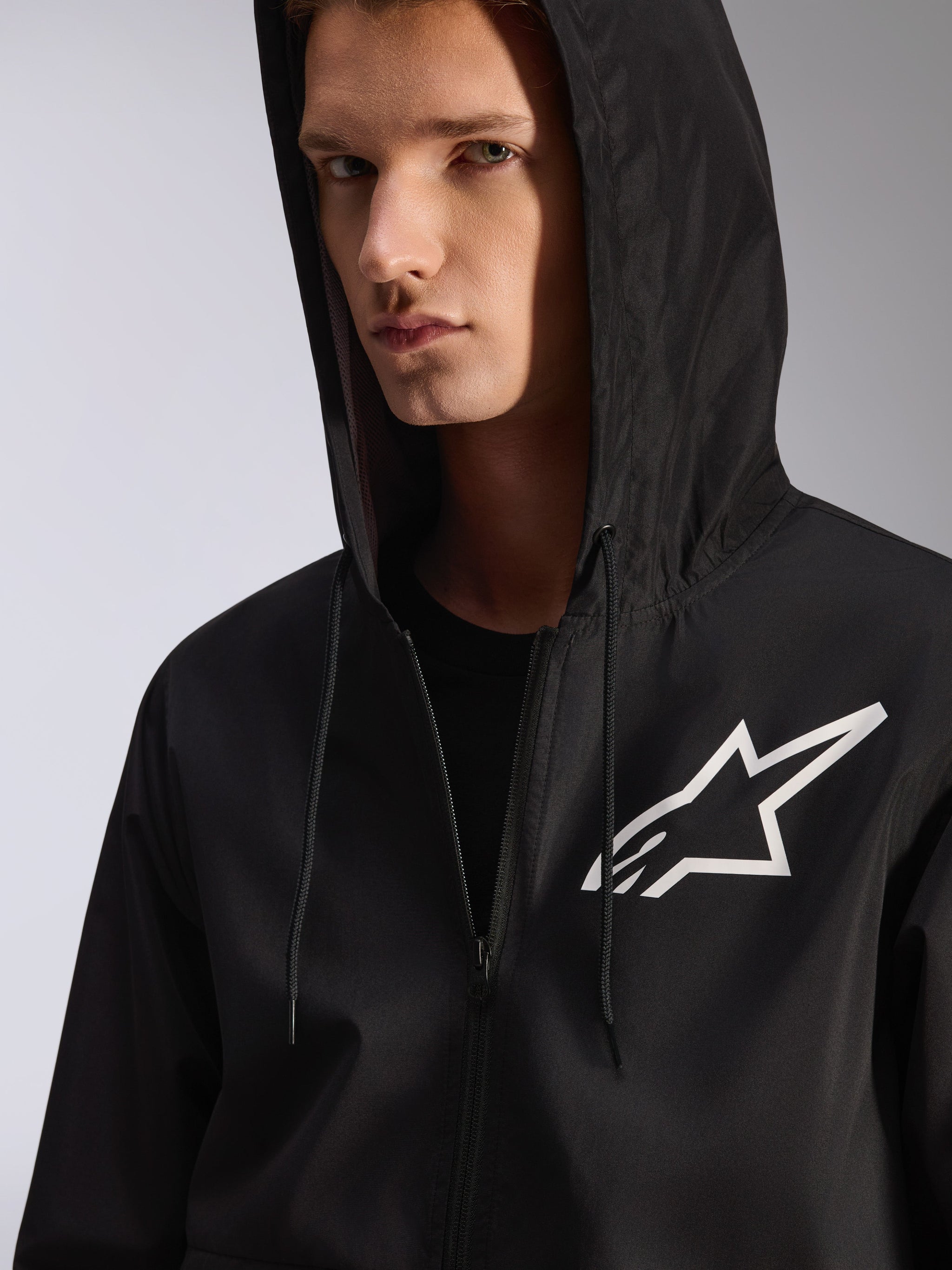 Alpinestars Speeder Chromium Windbreak Jacket, Black, close-up of a hooded windbreaker with a white star logo on the chest, features a drawstring hood, lightweight textile material, casual motorsport-inspired streetwear