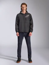 Alpinestars Speeder Chromium Windbreak Jacket, Black with White Astars Logo, worn by model with dark blue jeans and black sneakers, featuring a hooded design and front zipper, casual motorsport-inspired streetwear