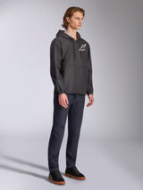 Alpinestars Speeder Chromium Windbreak Jacket, Black, hooded windbreaker with front zipper, white Alpinestars star logo on the left chest, casual motorsport streetwear, styled with dark pants and black sneakers in a studio setting.