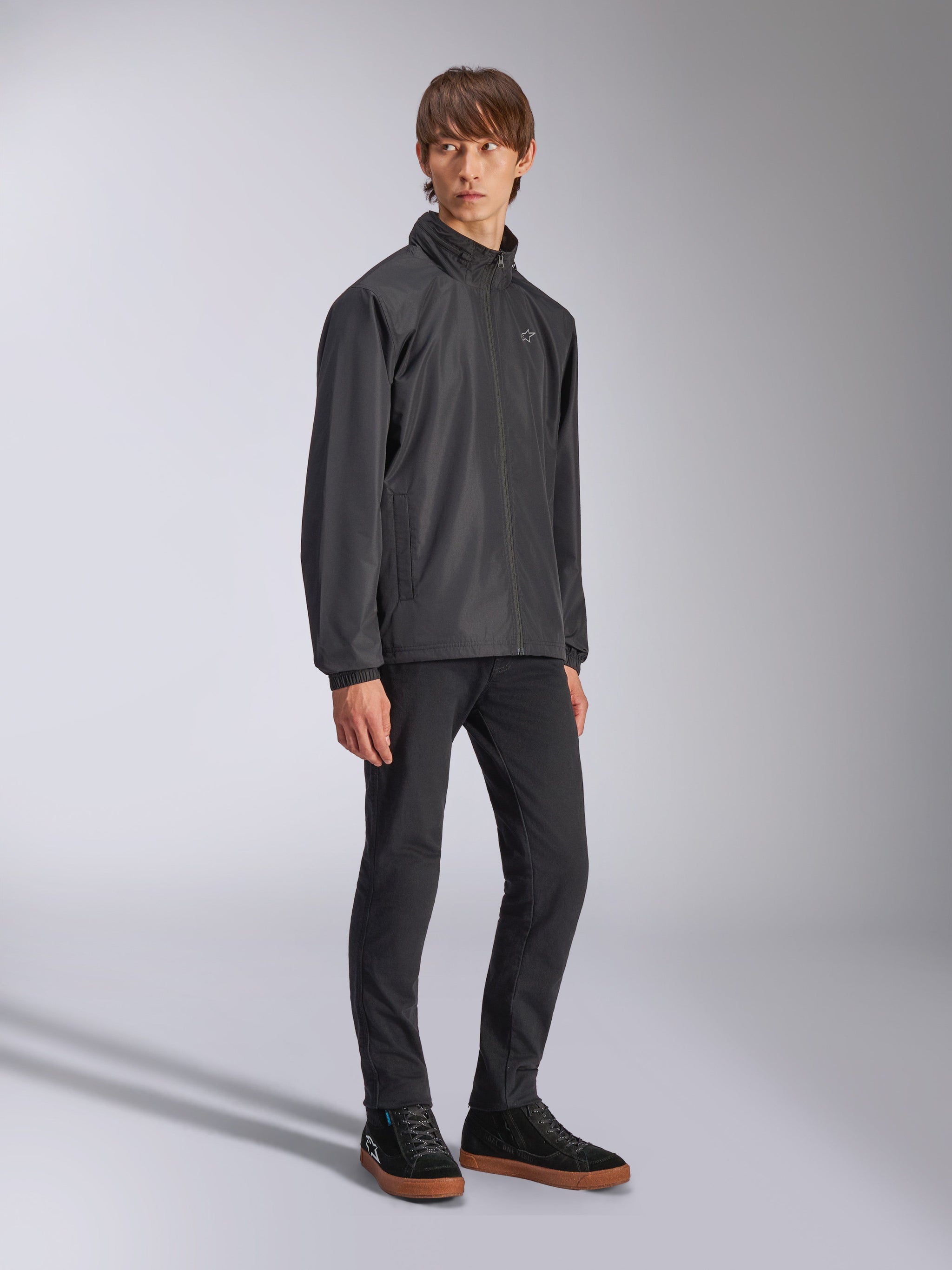 Alpinestars Overhaul Racer Jacket, Black rain shell jacket, worn with black trousers and black sneakers with gum soles, featuring a white star logo on the chest, zip-up front, casual motorsport-inspired sportswear