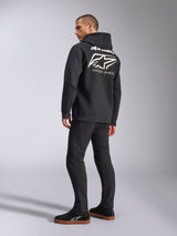 Model wearing Alpinestars Formulation Hoodie, Black, back view featuring large white Alpinestars logo and 'RACING AHEAD' wordmark, casual motorsport-inspired streetwear paired with black pants and black sneakers