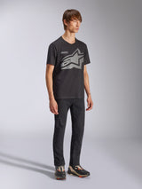 Male model wearing Alpinestars Fasting CSF Tee, Short Sleeve T-Shirt, Black, front grey Astars geometric star logo with Forward Innovation text, paired with black pants and sneakers, Casual Sportswear Lifestyle