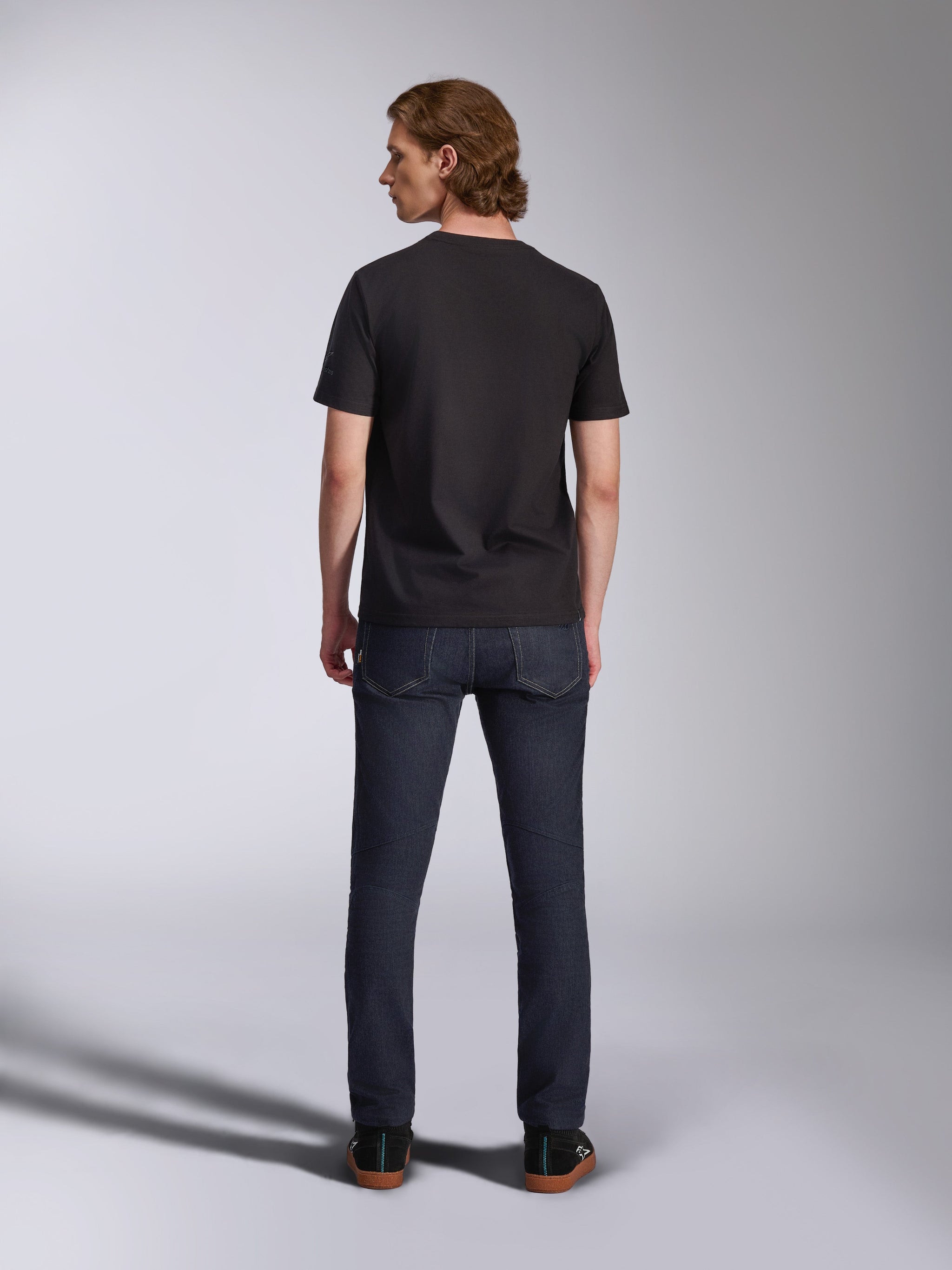 Alpinestars Global CSF Tee, Short Sleeve T-Shirt in Black, back view of male model wearing the shirt with dark denim jeans, casual motorsport-inspired streetwear