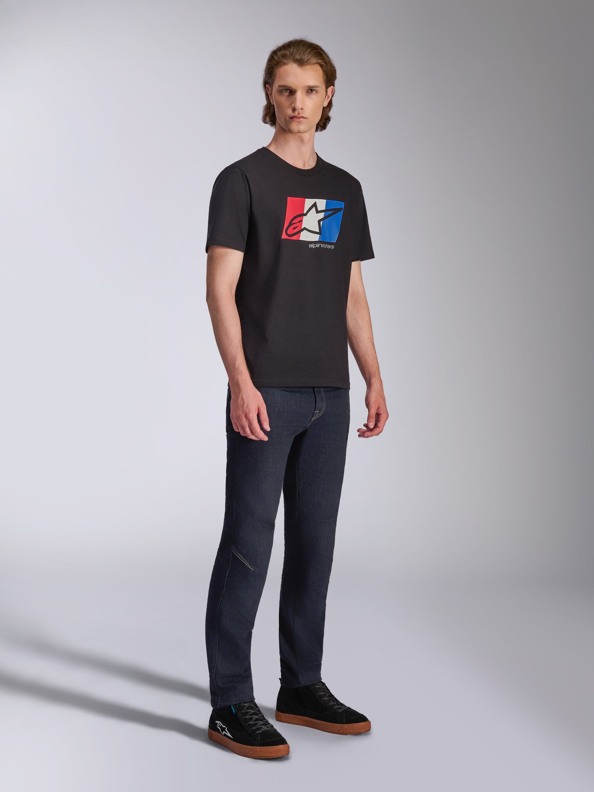 Alpinestars Global CSF Tee, Short Sleeve T-Shirt, Black with Red White and Blue Logo Graphic, Casual Motorsport Streetwear, Full body shot of model wearing dark jeans and black sneakers