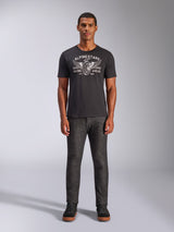 Alpinestars Heritage Patch CSF Tee, Short Sleeve T-Shirt, Black, featuring a white winged wheel graphic with 'Racing Ahead' text, worn by a model with dark grey pants and black sneakers, Casual Motorsport Streetwear