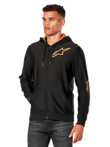 Alpinestars Sessions V3 Hoodie, Black with Gold logos, zip-up fleece hoodie worn by a model with dark jeans, featuring a gold mesh-lined hood and red-tipped drawcords, casual motorsport-inspired streetwear