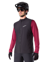 Alpinestars A-Dura Thermal Vest, Black, Cycling Thermal Gilet, worn over a maroon long-sleeve shirt, featuring a white chest logo, paired with a black MTB helmet and sunglasses, insulated performance layer for mountain biking