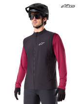 Alpinestars A-Dura Thermal Vest, men's mountain biking thermal vest in black, worn by a model with a helmet and a red long-sleeve jersey, insulation for cold-weather MTB riding