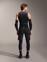 Alpinestars A-Motion Plasma Protection Vest, Back View, Black with Grey Camo shoulder accents, worn by model with black elbow guards, cycling shorts over leggings, and black riding shoes, showcasing the integrated back protector.