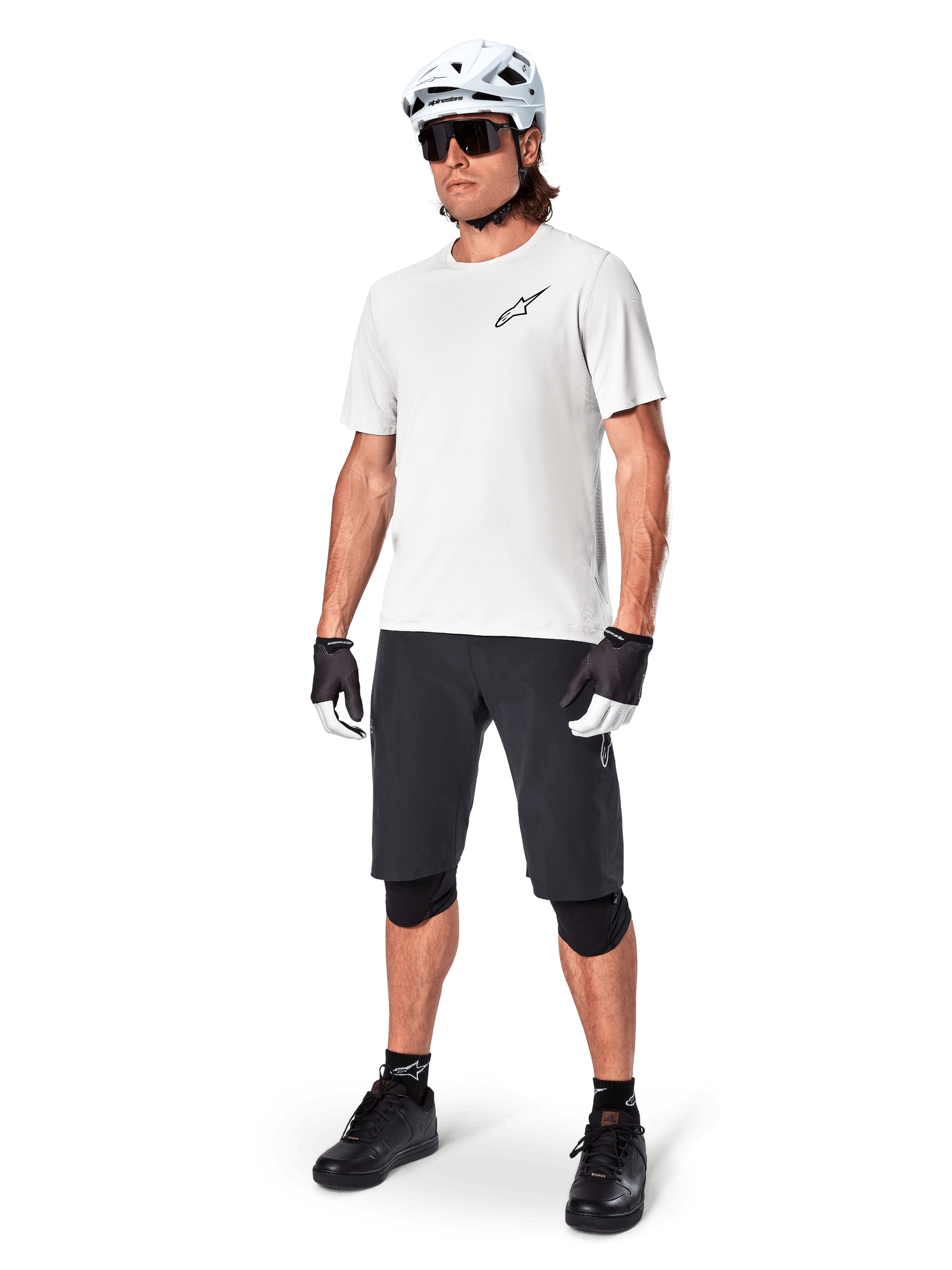 Male mountain biker wearing Alpinestars A-Aria Shorts, Black cycling shorts, styled with a white short-sleeve jersey, white mountain bike helmet, and black performance gear, full outfit for off-road trail riding