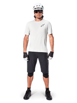 Male mountain biker wearing Alpinestars A-Aria Shorts, Black, paired with a white performance jersey, white helmet, and black knee protectors, professional off-road cycling gear in a full-body front view