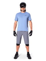 Male rider wearing Alpinestars A-Dura Shorts in Dark Gray, styled with a light blue short-sleeve t-shirt, black helmet, sunglasses, and black knee pads, complete mountain biking outfit for off-road performance.