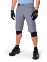 Alpinestars A-Dura Shorts, Dark Gray Mountain Bike Shorts, paired with black gloves and knee guards, featuring zippered pockets and double snap closure, rugged cycling gear for off-road trails