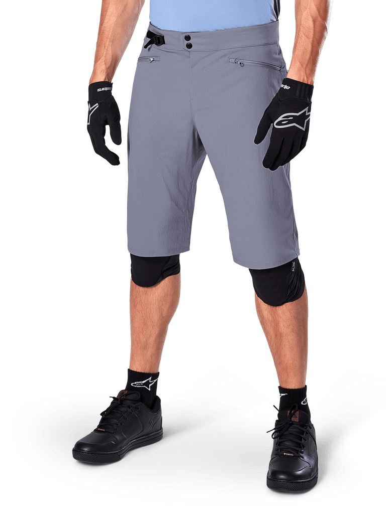 Alpinestars A-Dura Shorts, Dark Gray Mountain Bike Shorts, paired with black gloves and knee guards, featuring zippered pockets and double snap closure, rugged cycling gear for off-road trails