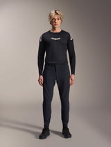 Male model wearing the Alpinestars A-Aria Polartec Elite Long Sleeve Jersey in Black, featuring a white Astars logo on the chest and shoulder branding, paired with black technical MTB pants and shoes, performance mountain bike gear
