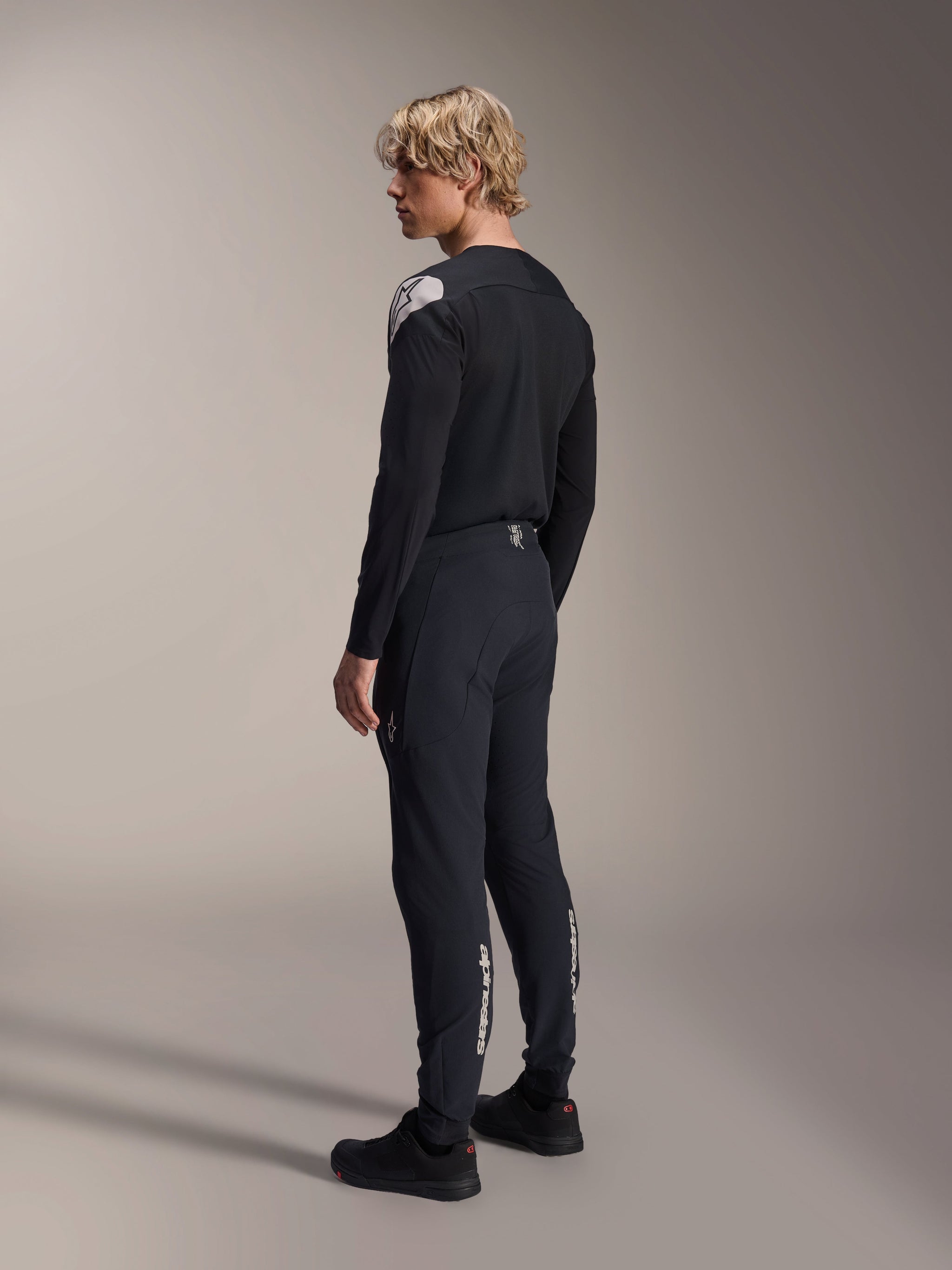 Alpinestars A-Aria Elite Pants, Mountain Bike Pants, Black Titanium, rear three-quarter view on model, featuring white Alpinestars branding on the lower legs, performance fit with elastic cuffs, paired with a matching black long-sleeve jersey.