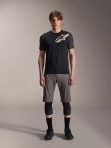 Alpinestars A-Dura Lipan Short Sleeve Jersey, Black with grey marl sleeves and tan Astars chest logo, worn by a male model with grey mountain bike shorts and black knee guards, performance MTB riding gear.