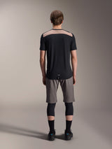 Alpinestars A-Dura Lipan Jersey - Short Sleeve, Black with tan upper back panel, rear view showing dropped tail, worn with grey MTB shorts and black knee guards, performance mountain bike apparel