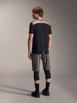 Alpinestars A-Dura Lipan Short Sleeve Jersey in Black, back view on model showcasing the light brown perforated mesh panel across the upper back, paired with grey mountain bike shorts and black knee guards for a complete trail riding outfit.