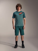 Alpinestars A-Dura Shorts in Dark Pine, men's mountain bike shorts, shown on a model with a matching teal short-sleeve jersey featuring a red and black star logo, black socks and cycling shoes, casual sporty mountain biking apparel