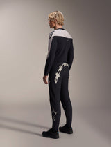 Alpinestars A-Supra Melt Long Sleeve Jersey, Black with white shoulder panels, worn by a model from the back and side, paired with black mountain bike pants featuring a large white wordmark, performance MTB racing kit