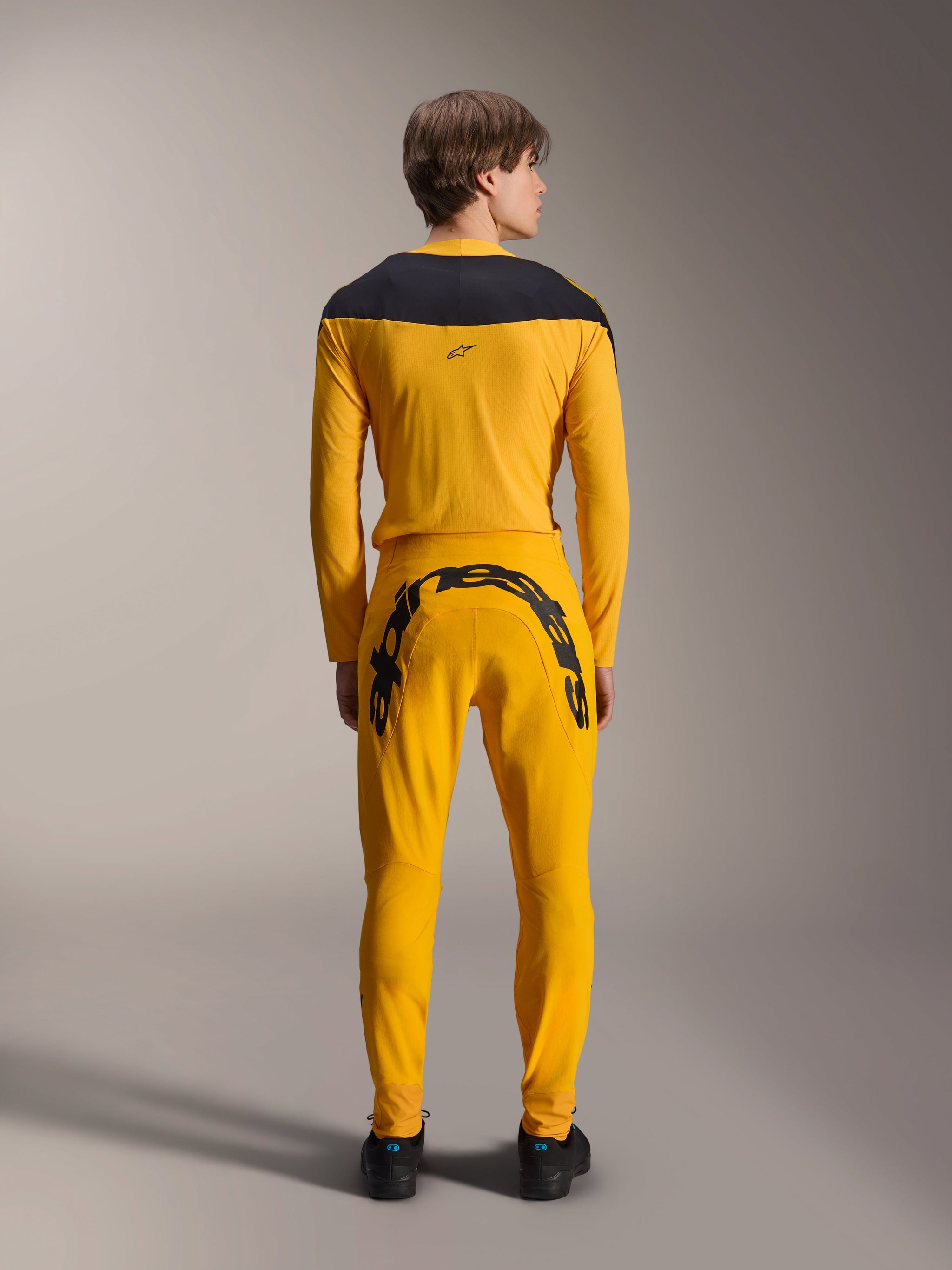 Alpinestars Limited Edition A-Supra Melt Gold Jersey, Long Sleeve MTB Jersey, Dark Yellow, back view, featuring black shoulder panels, worn with matching yellow pants with large black branding on the rear, performance cycling gear