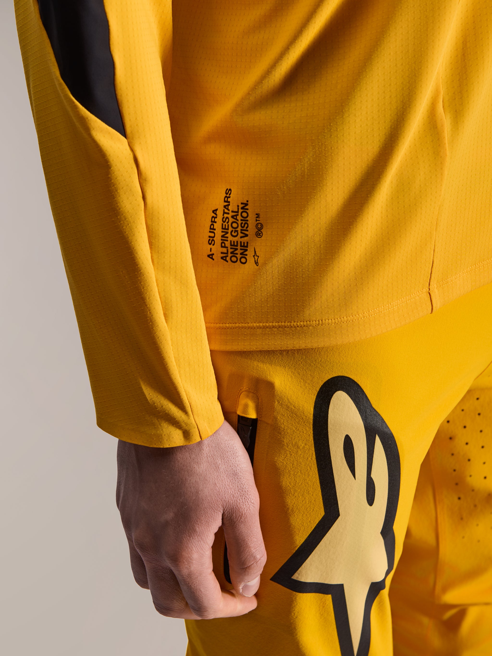 Alpinestars Limited Edition A-Supra Melt Gold Gear-Set, close-up of dark yellow long-sleeve jersey and matching pants, featuring 'One Goal. One Vision.' branding and large Astars logo, micro-perforated technical fabric for MTB racing