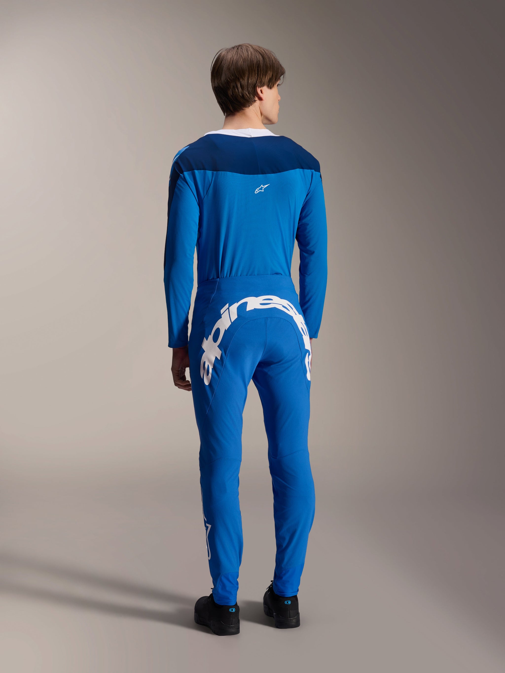 Male model seen from the back wearing the Alpinestars A-Supra Melt Long Sleeve Jersey in Blue, paired with matching blue performance pants featuring a large white Alpinestars wordmark across the back, complete MTB racing kit.
