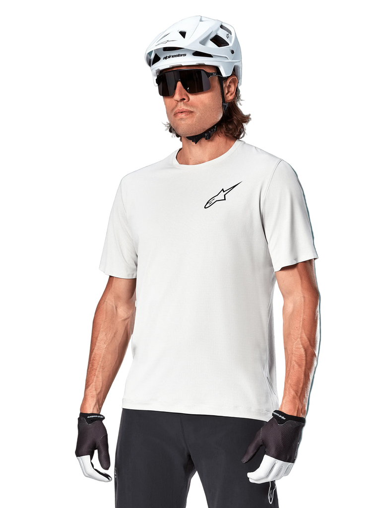 Alpinestars A-Aria Astar Short Sleeve Jersey, White Dove, worn by a cyclist with a white helmet and dark sunglasses, featuring a small black star logo on the chest, breathable performance gear for mountain biking