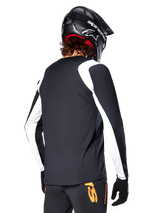 MTB rider wearing Alpinestars A-Supra Oscar Long Sleeve Jersey, Black with white panels on the shoulders and sleeves, viewed from behind, black helmet and gloves, pants with orange accents, durable off-road cycling apparel