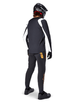Alpinestars A-Supra Oscar Long Sleeve Jersey, Black with white panels on sleeves, worn by an MTB rider from the back with a black full-face helmet and black pants featuring orange logos, cycling apparel for off-road gravity riding