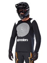 Alpinestars A-Supra Oscar Long Sleeve Jersey, MTB Cycling Jersey, Black and White, featuring a bold white spiral design and Alpinestars logo on the chest, worn with a black full-face helmet and goggles, performance mountain biking apparel