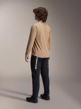 Alpinestars A-Dura Astar Long Sleeve Jersey in Light Brown, back view of a male model showcasing the drop tail design, paired with black pants and shoes, casual mountain bike performance gear.