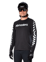 Alpinestars A-Dura Dri Oscar Long Sleeve Jersey, MTB Cycling Jersey, Black Reflective, featuring a white chest wordmark and bold reflective circular graphics on the sleeves, worn with a black helmet and sunglasses, technical moisture-wicking apparel for off-road mountain biking