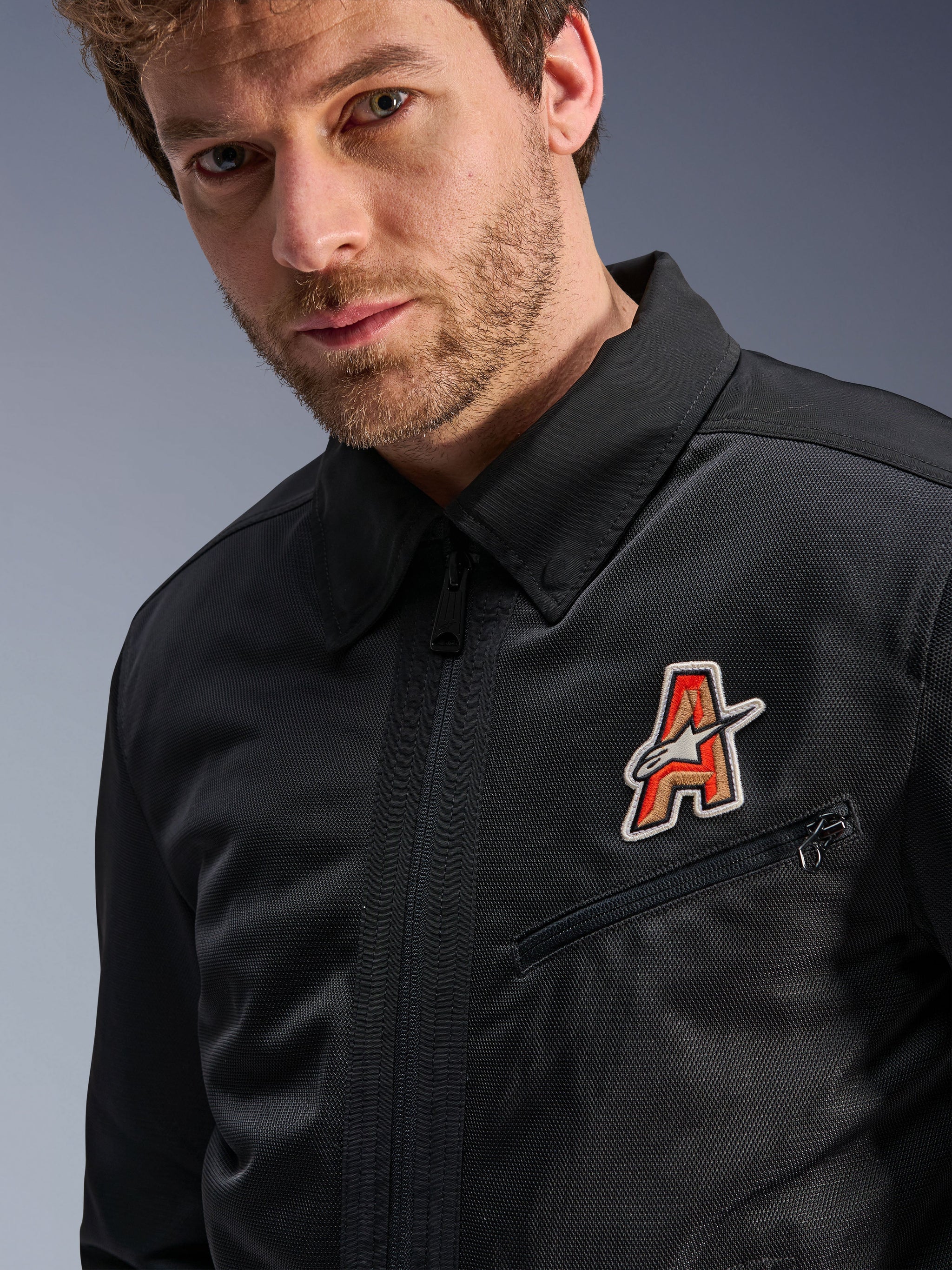 Alpinestars Ignite Air Jacket, Black, featuring a traditional shirt collar and breathable mesh construction, highlighted by a red and gold 'A' logo patch on the chest, worn by a male model, urban motorcycle apparel