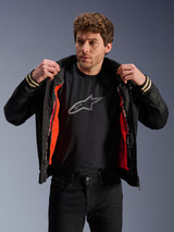 Man wearing Alpinestars Ignite Air Jacket, Black, featuring a mesh body and bright orange detachable windproof liner, paired with a black Astars logo t-shirt and black pants, urban contemporary motorcycle style