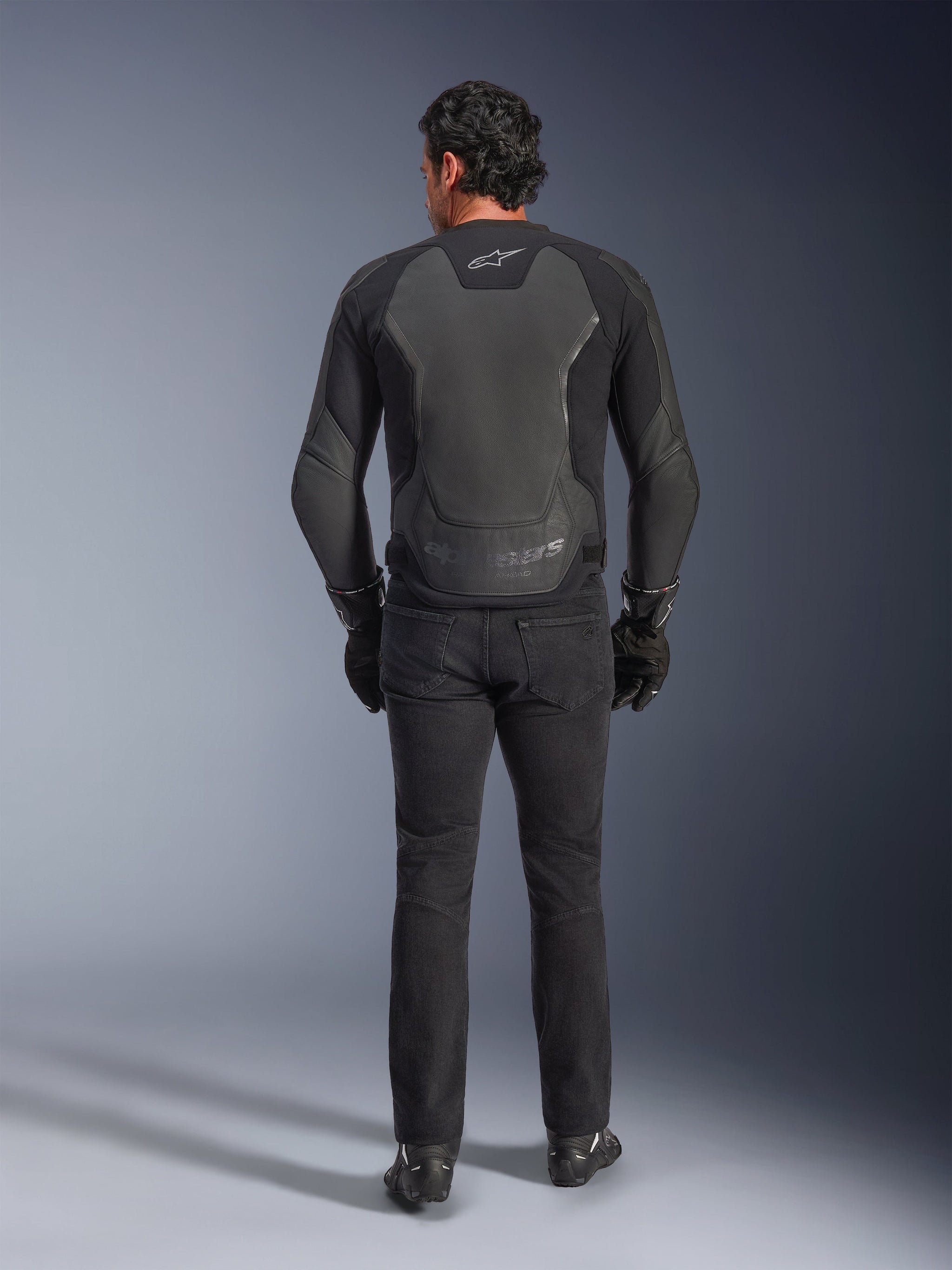 Alpinestars GP Force V2 Leather Jacket, Black, back view, premium sport motorcycle jacket with leather-textile construction, worn with black riding jeans and gloves, featuring protective shoulder panels and branding details