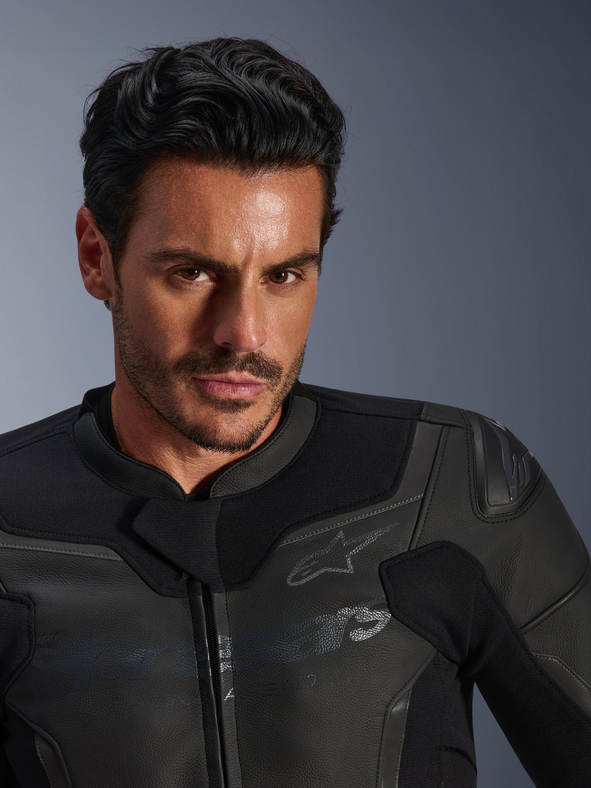 Close-up portrait of a male model wearing the Alpinestars GP Force V2 Leather Jacket, Black, featuring premium bovine leather construction, textile stretch panels, and a subtle Alpinestars star logo, sleek sport-focused design for road riding.