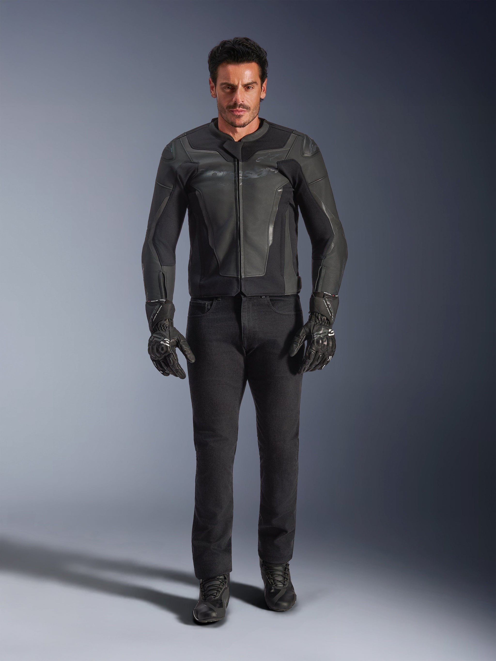 Alpinestars GP Force V2 Leather Jacket in Black, worn by a male rider with black motorcycle pants, gloves, and boots, sleek sport-style leather construction with shoulder sliders and integrated protection.