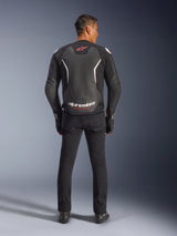 Alpinestars GP Force V2 Leather Jacket, Black and White, rear view, worn by a rider with black pants and gloves, featuring large white branding on the lower back and red accents, premium bovine leather construction for motorcycle road gear
