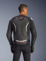 Alpinestars GP Force V2 Leather Jacket, Rear view, Black and White, featuring red star logo on the upper back and white Alpinestars branding with 'Racing Ahead' text, worn with black pants and matching gloves, sport-fit leather motorcycle jacket