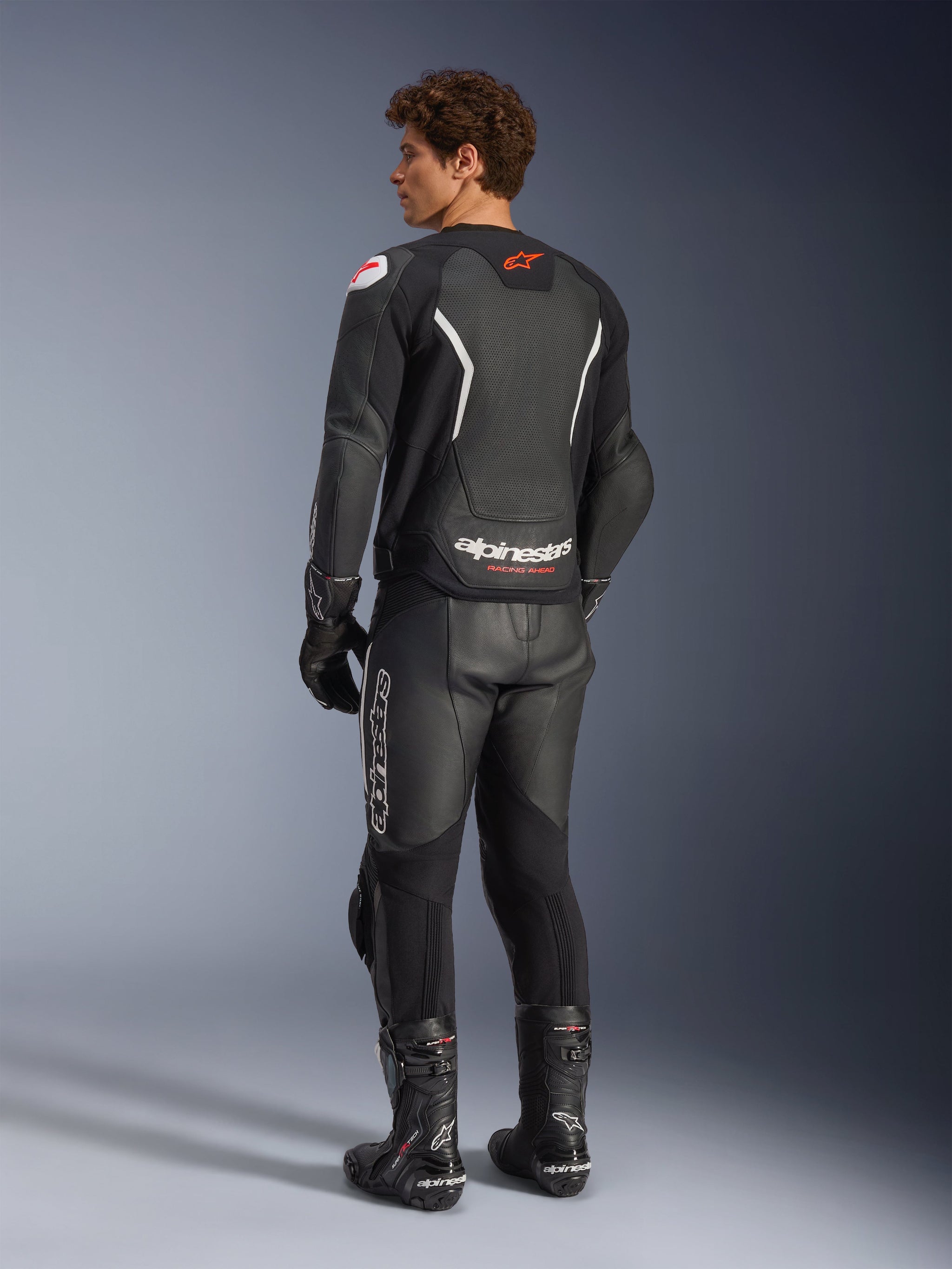Alpinestars GP Force V2 Air Leather Jacket, Black and White, rear view on model featuring perforated back panel for ventilation, white branding and red star logo, worn with matching leather racing pants, gloves, and boots